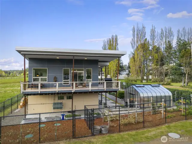 Full backyard view with beautifully landscaped gardens, greenhouse, and fenced yard.