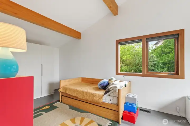 Second upstairs bedroom with vaulted ceilings and a cheery green view outside the window.