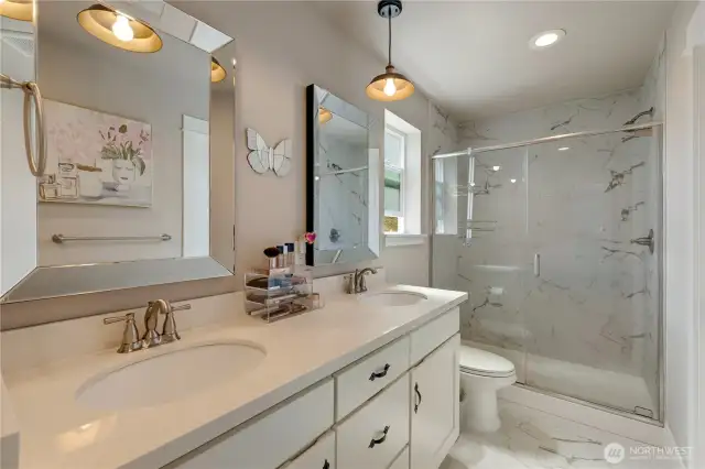 Primary bath with quartz countertops, pendant lightning and walk-in tile shower.