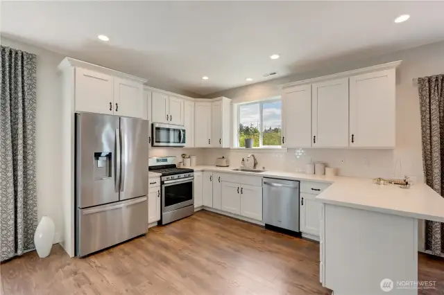 Beautiful open kitchen with quartz counters, SS appliances, and white shaker cabinets.