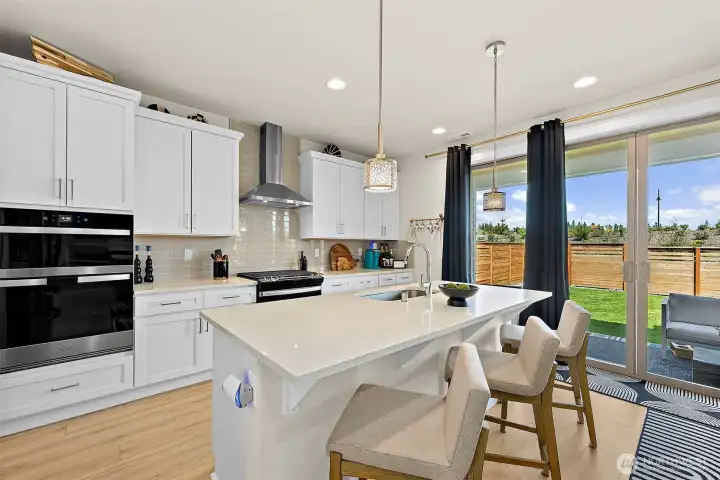 Large kitchen island, gas range, double oven with a walk-in pantry just steps away to the left of frame.