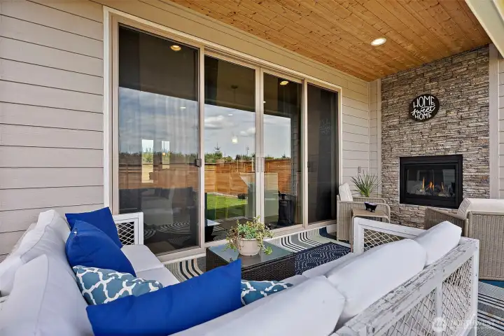 Just beyond the kitchen is the covered outdoor living space upgraded with finished wood soffit/ceiling and elegant stacked stone full height gas fireplace wall.