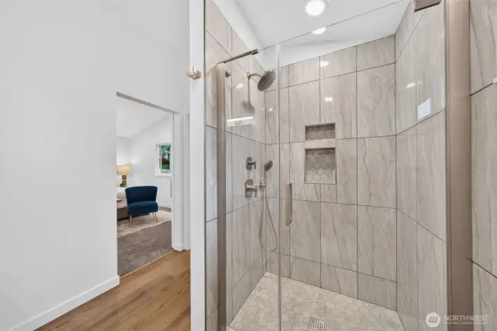 A beautifully tiled walk-in shower with polished nickel finishes, built-in niches, and a handheld showerhead—clean, modern, and made for everyday luxury.