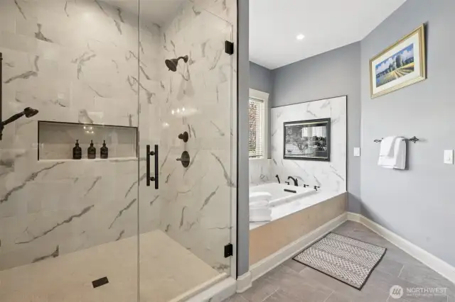 Indulge in everyday serenity within this spa-style ensuite, where an oversized glass-enclosed shower with dual showerheads meets a jetted soaking tub framed by porcelain marble tile. A double-sided gas fireplace adds ambiance from both the bath and bedroom, elevating relaxation with a warm, luxurious glow. Soft natural light and sophisticated finishes invite you to linger a little longer.