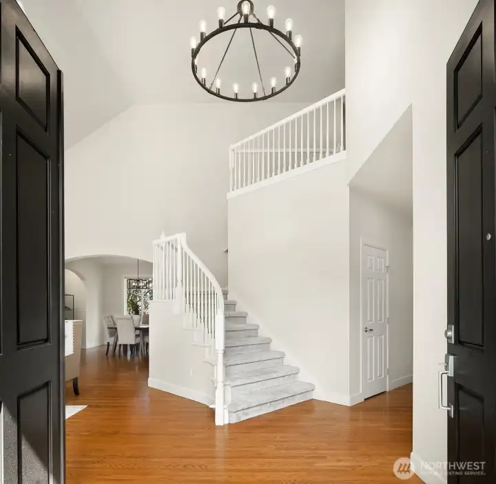 This grand two-story entry foyer makes an immediate statement with soaring vaulted ceilings, an elegant chandelier, and rich hardwood floors that set the tone for the refined finishes found throughout the home. The bright, airy space and beautifully crafted staircase create a warm and welcoming first impression the moment you step inside.