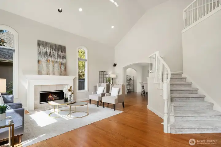 The elegant living room impresses with soaring vaulted ceilings, a classic white fireplace surround, and rich hardwood floors that flow seamlessly throughout the main level. Bathed in natural light and framed by beautiful architectural details, this sophisticated yet comfortable space is perfectly suited for both relaxed everyday living and gracious entertaining.
