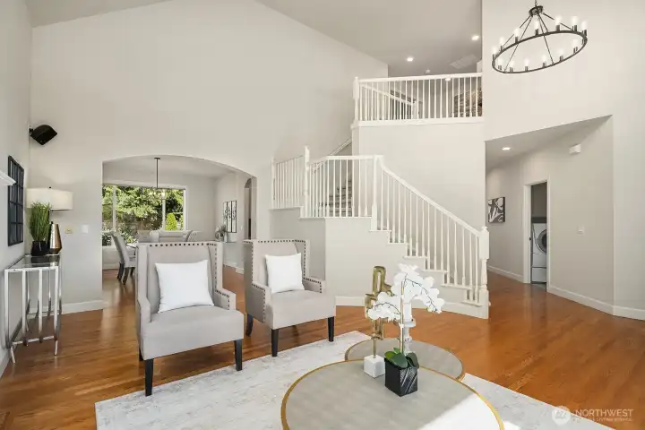 This beautifully composed view captures the seamless flow between the living room and the grand entry foyer, highlighting the home's stunning architectural details including elegant arched doorways, soaring ceilings, and gleaming hardwood floors. The open, light-filled layout and thoughtful design create a sense of spaciousness and sophistication that is evident throughout the entire main level.