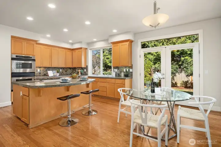 This well-appointed kitchen features warm wood cabinetry, granite and slate countertops, stainless steel appliances, and a central island with bar seating — offering both exceptional functionality and a welcoming space for casual dining. A bright garden window, updated lighting, and seamless flow into the dining area make this kitchen as practical as it is charming.