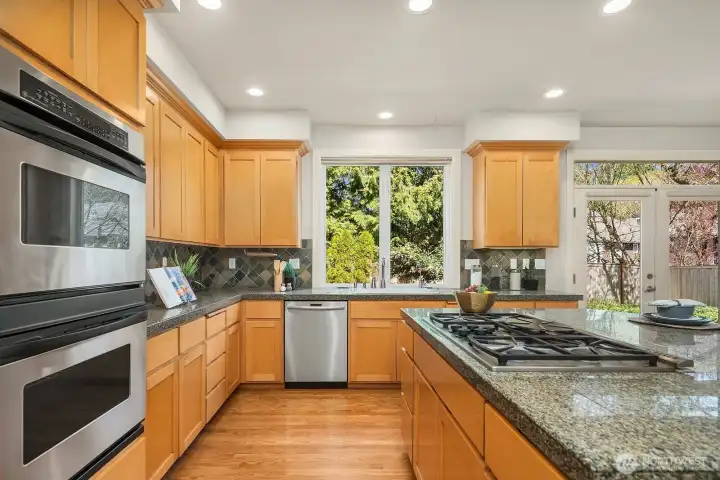 A closer look at the kitchen reveals beautiful granite and slate countertops, rich wood cabinetry with abundant storage, and premium stainless steel appliances including double wall ovens — a true chef's delight. The large window above the sink frames a lovely garden view, filling this thoughtfully designed workspace with natural light and bringing the outdoors in.