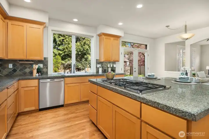 This alternate view highlights the kitchen's generous layout, showcasing the expansive granite and slate countertops, abundant cabinetry, and large windows that flood the space with natural light and offer peaceful garden views. The premium stainless steel appliances, ample prep space, and seamless flow make this kitchen perfectly equipped for both everyday cooking and entertaining on any scale.