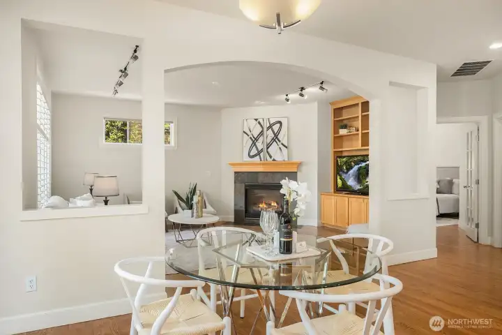 This charming view captures the seamless connection between the casual dining nook and the family room beyond, featuring elegant arched built-ins flanking the fireplace and rich hardwood floors that unify the space. The open, flowing layout and abundance of natural light make this area the true everyday heart of the home, perfect for relaxed family gatherings.