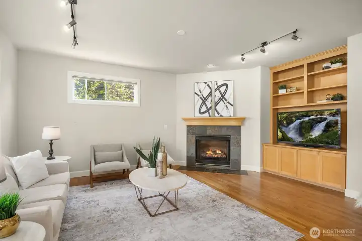 This alternate view of the family room showcases the elegant built-in shelving and cabinetry flanking the brick fireplace, offering both stylish display space and practical storage that adds tremendous character to the room. The hardwood floors, abundant natural light, and open flow to the adjacent kitchen and dining areas make this space as functional as it is inviting.