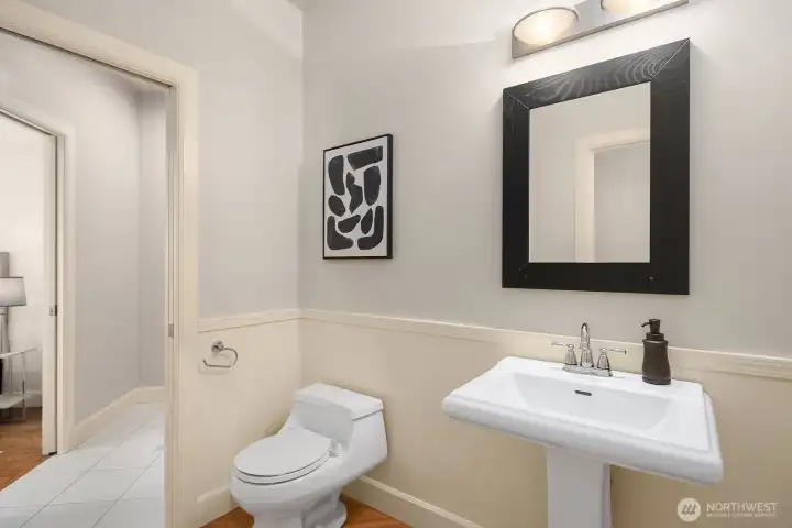 This crisp and elegantly appointed powder room features a classic pedestal sink, bold framed mirror, and refined neutral finishes that reflect the thoughtful attention to detail found throughout the home. Conveniently located on the main level, this stylish space makes a polished impression on guests while serving everyday needs with understated sophistication.