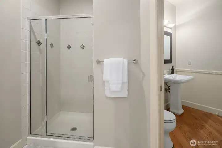 This clean and well-appointed main level three-quarter bath features a sleek walk-in shower with frameless glass enclosure, offering convenient private access for the main level bedroom guest suite. The fresh, neutral finishes and quality fixtures make this practical bathroom both functional and move-in ready.