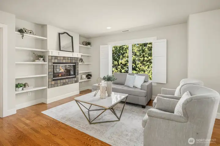 This alternate view of the primary suite's sitting room showcases the elegant dual-sided fireplace flanked by beautiful built-in shelving, creating a sophisticated and cozy retreat within the suite itself. The hardwood floors, large garden-facing windows, and refined finishes make this exceptional space feel more like a private luxury lounge than a bedroom sitting area.