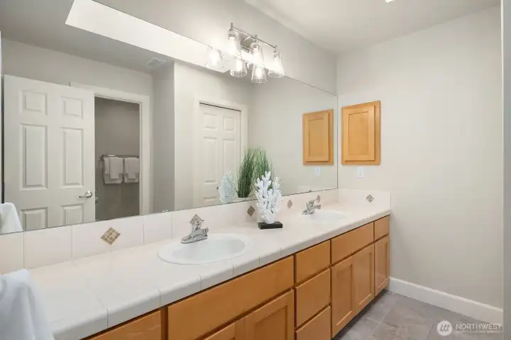 This well-appointed upper level full hall bath features dual vanities with ample counter space, warm wood cabinetry, and clean, neutral finishes that serve the additional upper level bedrooms with both comfort and practicality. Thoughtfully designed to accommodate busy morning routines, this generously sized bath is a highly functional and welcome amenity for family living.