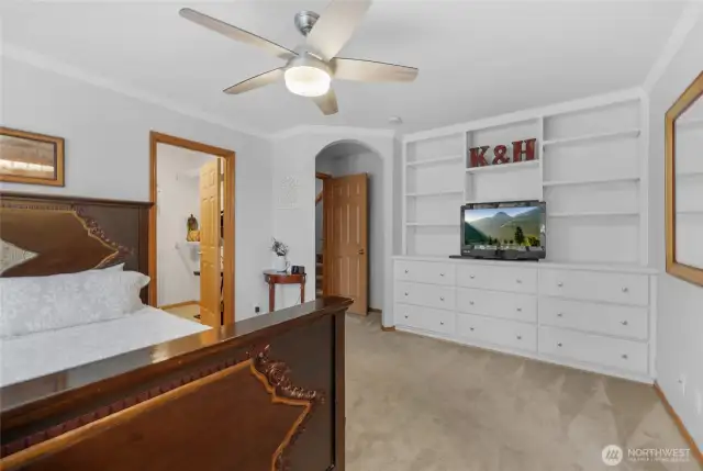 MAIN FLOOR primary bedroom is large with built-in dresser and shelving area. There are also large windows looking into the backyard. The bedroom has a ceiling fan, a walk-in closet, and an attached five-piece bathroom