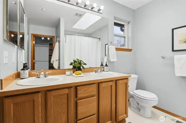 Double sink vanity in primary bathroom and a large walk-in closet with custom shelving.
