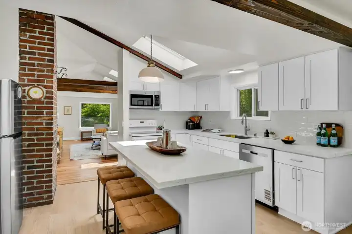 Open-concept kitchen featuring skylights, exposed beams, island seating, and seamless indoor-outdoor flow. Open-concept kitchen featuring skylights, exposed beams, island seating, and seamless indoor-outdoor flow.