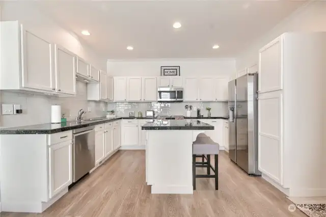 Gorgeous kitchen with slab granite counters, updated cabinets, stainless steel appliances, under cabinet lighting, center island with eating bar, full height backsplash.