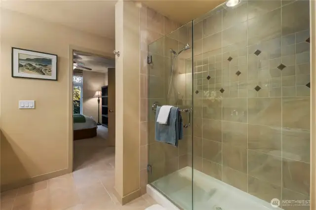 The primary bathroom features a sleek walk-in shower enclosed in clear glass, offering a modern and open feel. Inside, the wall-mounted detachable shower wand provides both flexibility and convenience, ideal for a spa-like experience.