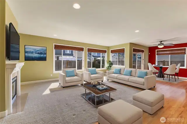 The great room offers a comfortable and inviting space with a cozy gas fireplace framed by a classic white mantle and tile surround. Large windows provide plenty of natural light and a lovely view of the fenced, landscaped backyard.