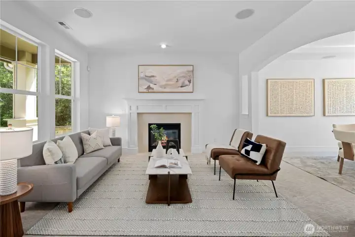 From the foyer, an arched entryway to the left opens into the formal living room, where the centered fireplace gives the room a formal yet welcoming presence. A clean white mantel, classic Craftsman style casing, and soft tile surround draw the room together, while large windows bring in natural light and frame the gardens outside. Imagine welcoming guests and family here, with the room setting the tone in soft, understated elegance.