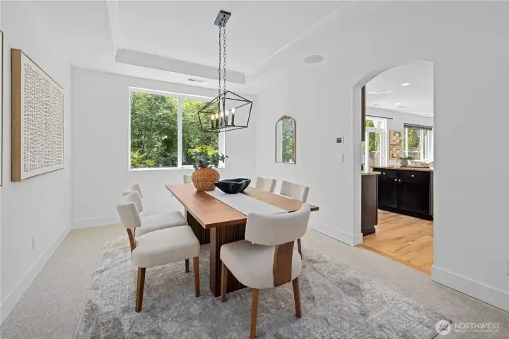 The formal dining room has a quiet, polished charm, with a tray-style ceiling and long cage lantern chandelier giving the space a gentle sense of occasion. The large window brings the backyard view into the room, while the doorway to the kitchen keeps everything close for shared meals, easy conversation, and evenings that linger a little longer.