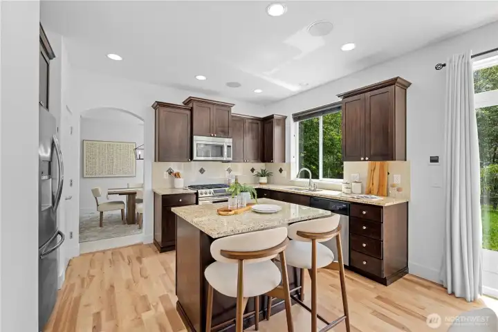 Cherry-toned Shaker-style cabinets bring warmth and structure to the kitchen, while generous storage wraps the room on multiple sides. The center island adds easy prep space right where it is needed most, with seating that keeps conversation close as meals come together.