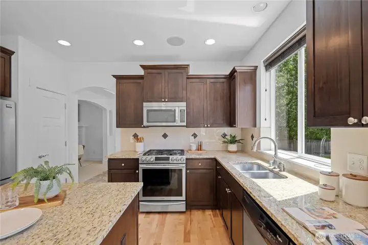 Warm speckled granite slab counters bring soft gold, cream, and charcoal tones through the kitchen, pairing beautifully with the cherry-toned cabinetry. The full height tile backsplash adds an elegant layer behind the range, with small decorative accent tiles giving the room just enough detail and rhythm. Multiple outlets allow for a variety of small appliances to assist in any whimsical meal creation.