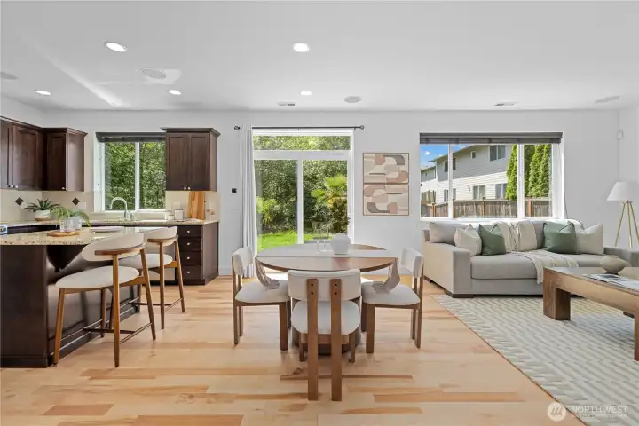 Sliding glass doors expand the living space to the outdoors, opening to the expansive rear patio and backyard. The extra glass panel above brings in even more light, and an iron cage-style curtain rod echoes the elegant chandelier in the dining room, carrying that detail softly from one space to the next. Southern exposure fills the open kitchen and family rooms with natural light, turning them warm and golden toward sunset.