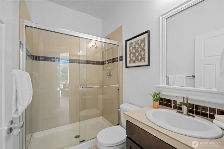 The main-floor three-quarter bath keeps everything easy for guests or the nearby bedroom, with a glass-enclosed shower that feels open, simple to step into, and easy to keep clean. Custom wrapped mirror frame adds an elegant touch. Warm ceramic tile continues the home’s soft neutral palette and quietly echoes the kitchen finishes for a connected, pulled-together feel.