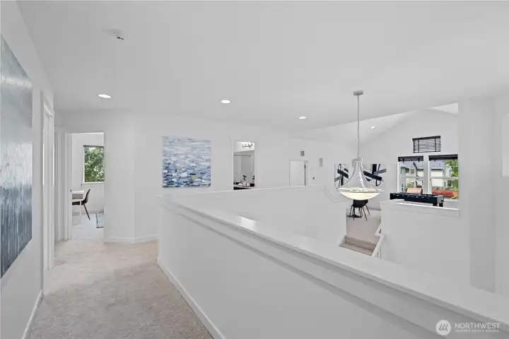 From the second-story hallway, the home feels elevated, open, and quietly connected to the spaces below. The open stairway keeps the landing light and airy, while recessed lights cast a soft, even glow along the hall. Natural light reaches in from the surrounding windows, and the modern glass bowl chandelier over the foyer adds a graceful focal point, floating below with a polished, sculptural feel.