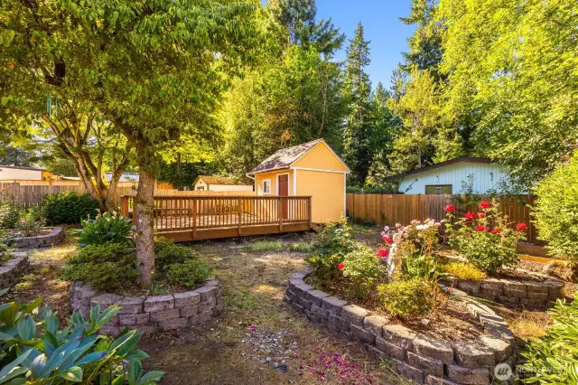 Large outbuilding with large wooden deck, flower beds, mature landscaping