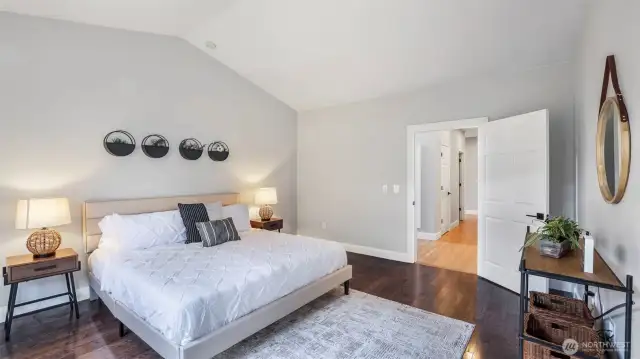This downstairs primary bedroom showcases soaring vaulted ceilings and elegant hardwood flooring!