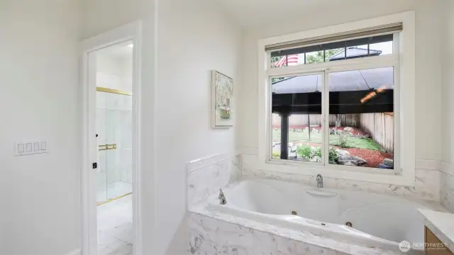 The en suite bathroom offers a spacious walk-in shower and separate toilet, a large soaking tub, and a huge window overlooking the backyard.