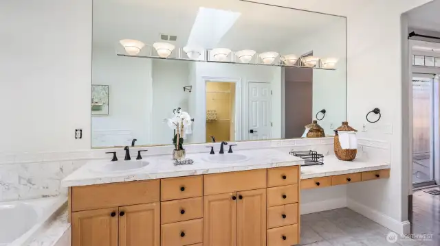 The wooden cabinet adds warm contrast to this modern en suite bathroom, which offers ample storage, a spacious countertop with two sinks, and a large mirror above