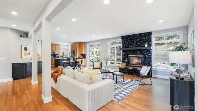 This vast open-concept space combines the living room, kitchen, dining area, and a charming nook—highlighted by warm wood flooring and a bold, stone-accented feature fireplace that adds character and charm