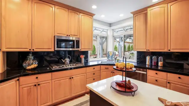 The kitchen showcases sleek black granite tile countertops, warm wood cabinetry, a spacious open layout, a double sink, a large window above the sink that brings in natural light, and a stylish backsplash
