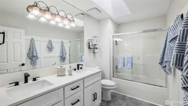 This upstairs full bathroom features a double sink with sleek white countertops and a skylight that fills the space with natural light