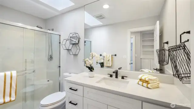 The second upstairs bathroom offers abundant storage, stylish white countertops, a spacious walk-in shower, a large mirror, and a skylight that brightens the room. This 3/4 bath combines function and natural light beautifully