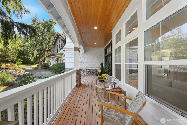 Newly refinished wraparound porch features rich wood flooring, crisp white railings, & serene views that invite relaxed outdoor living.