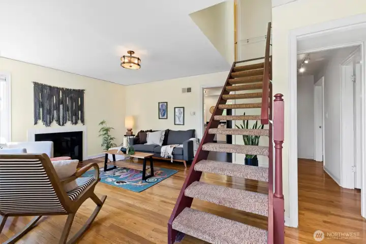 Bright and inviting living room with hardwood floors, fireplace, and an open staircase centerpiece.
