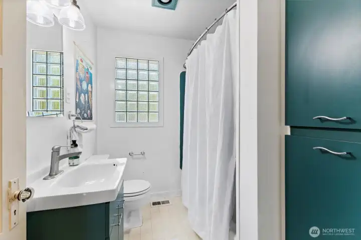 Main level full bathroom with modern fixtures, glass block window, and clean, bright design.