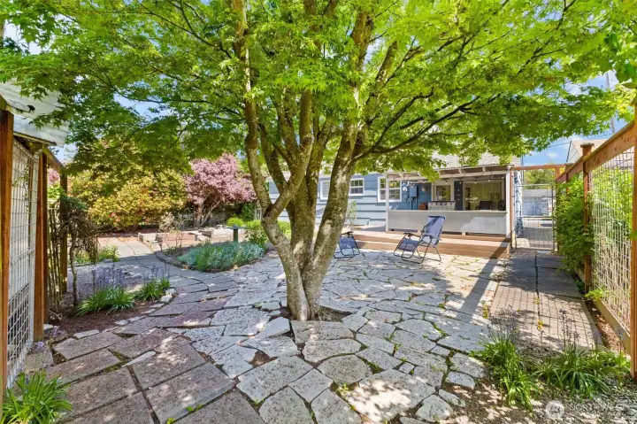 Private stone patio shaded by mature trees creates a peaceful setting for relaxing or entertaining.