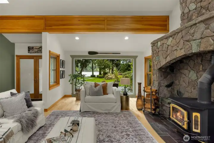 Generous living area with refinished hardwood floors, wood-burning stove, striking rock wall, vaulted ceilings, and exposed beams