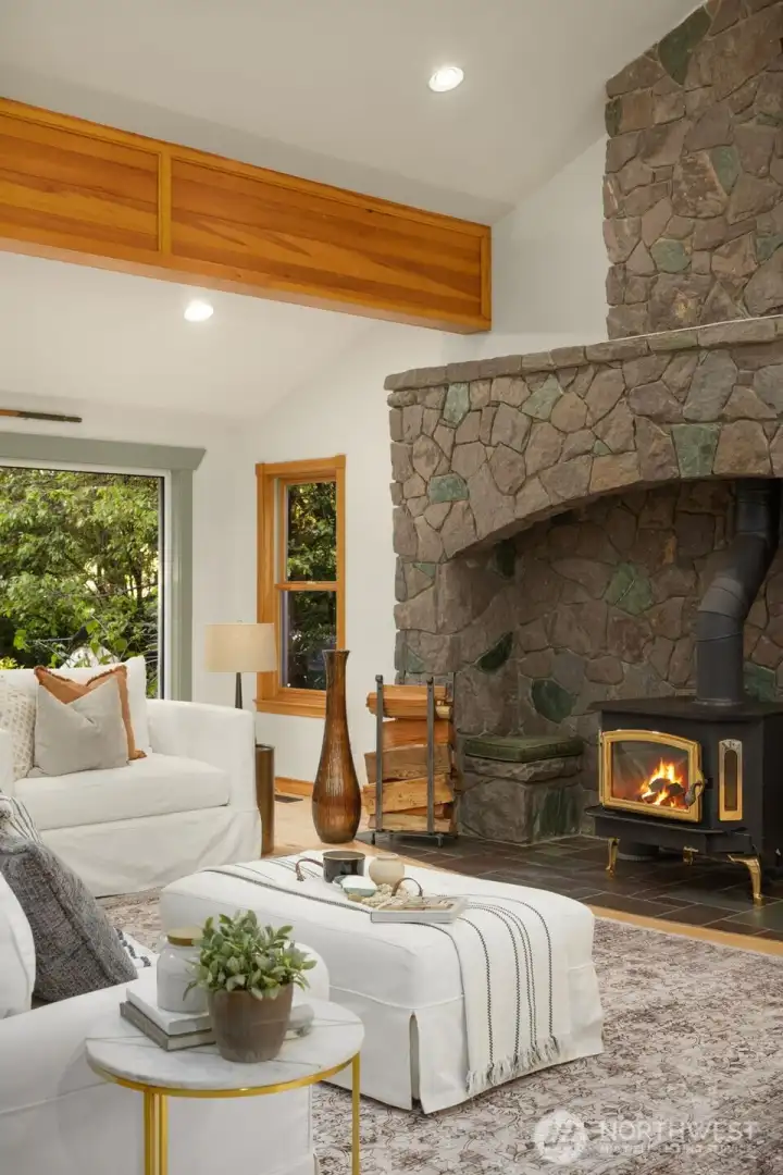 Generous living area with refinished hardwood floors, wood-burning stove, striking rock wall, vaulted ceilings, and exposed beams