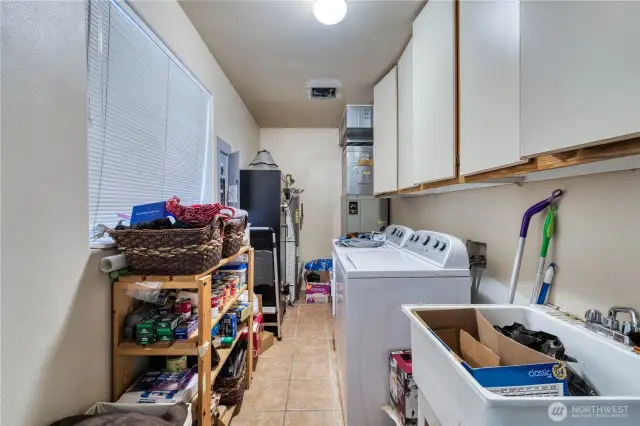 Laundry room has lots of room for additional storage, with cabinets and a deep sink.