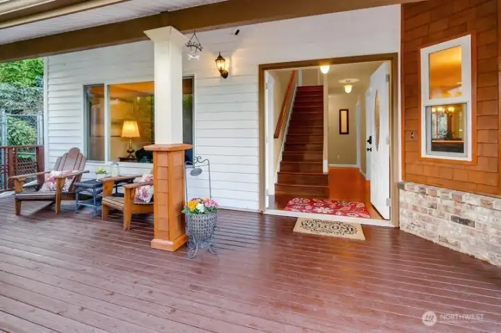 Covered front porch with wood deck, seating area. The French door entry leads to a well-lit foyer with hardwood floors, staircase, and hallway.