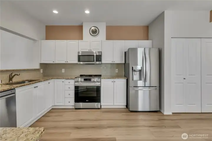 Big kitchen with white cabinets, granite, stainless steel appliances, tile backsplash, & new laminate floors
